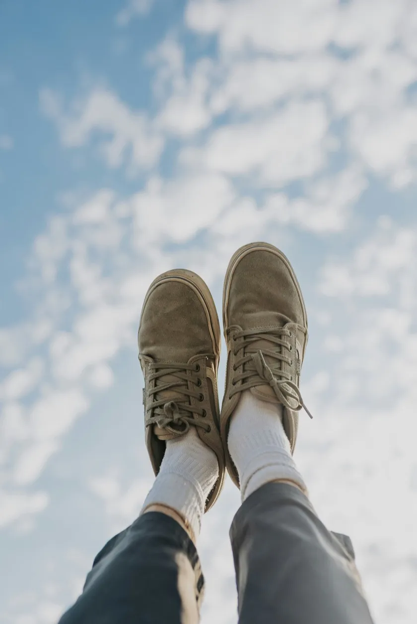 A person lying back with their feet raised against a bright, cloudy sky